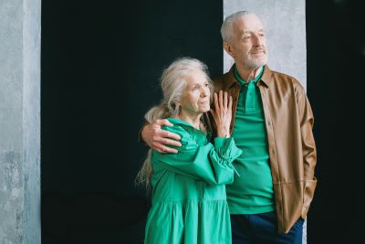 Older couple standing side by side, the man with his arm around the woman, both wearing green tops and looking into the distance.